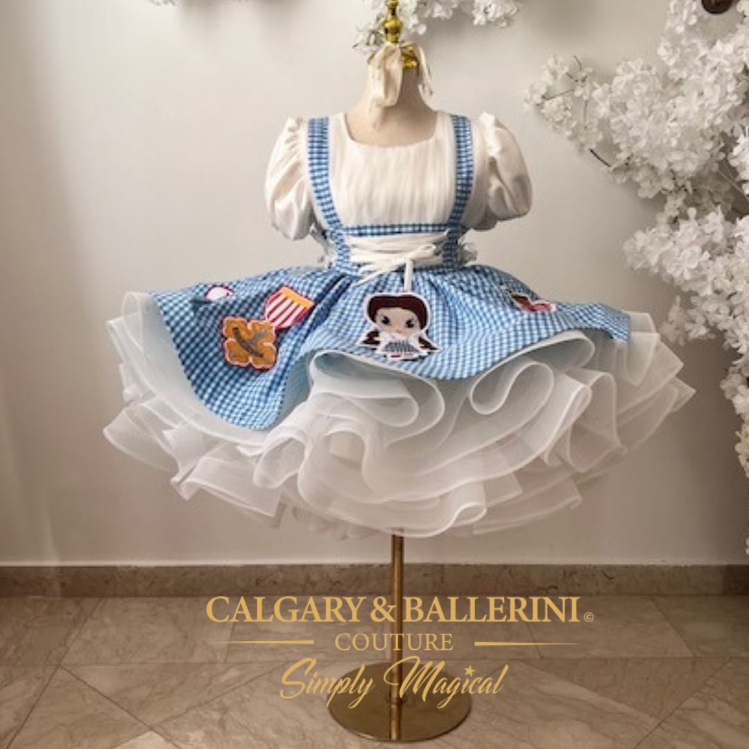 Order a bespoke Dorothy couture dress for first birthday parties, luxury handmade blue gingham gown with artisan character embroidery by Calgary and Ballerini.